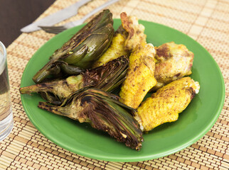 cooked fried chicken wings and halves artichokes on green plate