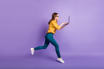 Full length profile photo of girl run hold pc typing touchpad wear yellow shirt blue pants sneakers isolated violet color background