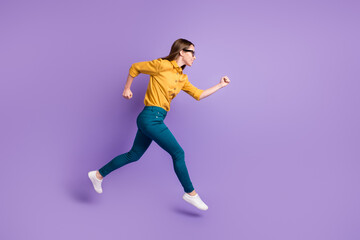 Fototapeta na wymiar Full length profile photo of girl run jump hurry wear yellow shirt blue trousers sneakers isolated purple color background