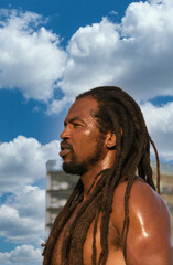 Picture of a shirtless African man in dreadlocks on a cloudy sky background