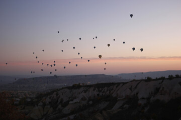 Colorful hot air balloons flying over mountains. Aerial view of a beautiful rocky landscape in the evening. Touristic place in Turkey.