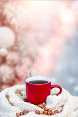 Red cup with coffee, tea on a snowy background, winter forest. A red cup against the background of a winter forest landscape on a soft, cozy scarf. Coffee, tea in the mountains.