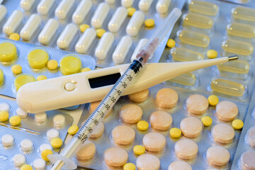 Thermometer and syringe on supplements and pills blister packs background. Pack of tablets.
