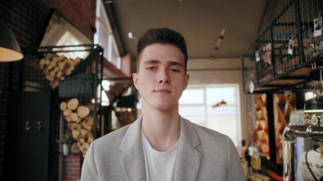 Close-up portrait of handsome young business man standing in coffee shop, looking at camera and smiling. Small business concept.