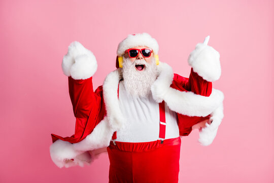 Photo of crazy funky cool grey bearded santa claus listen x-mas christmas holly music stereo sound headphones enjoy wear suspenders sunglass headwear isolated pastel color background