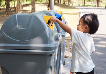 Little boy puts a plastic in to the trash in the park. Ecology, recycling and protection of nature...