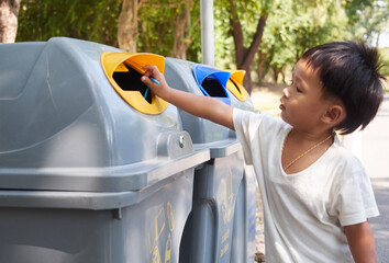 Little boy puts a plastic in to the trash in the park. Ecology, recycling and protection of nature...