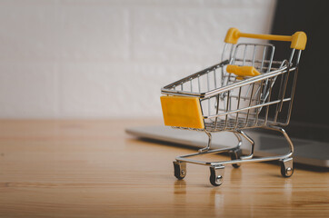 Shopping cart in with laptop on wood table in office background.Easy shopping with finger tips for consumers.concept of working at home through technology to shopping and sell things online.