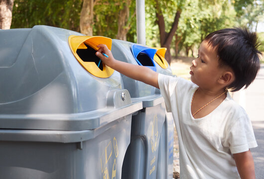 Little boy puts a plastic in to the trash in the park. Ecology, recycling and protection of nature concept.