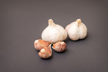Still life of two garlic heads and garlic cloves grouped on dark background