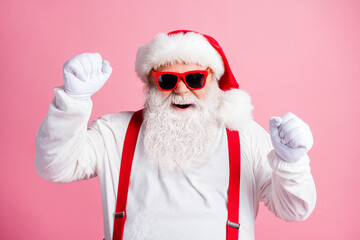 Photo delighted crazy santa claus raise fists enjoy rejoice x-mas christmas tradition discount lottery win wear style trendy sunglass suspenders gloves isolated pastel color background