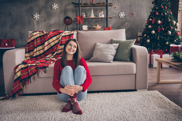 Photo of charming girl sitting carpet couch look up embrace legs wear red pullover socks jeans in decorated x-mas living room indoors