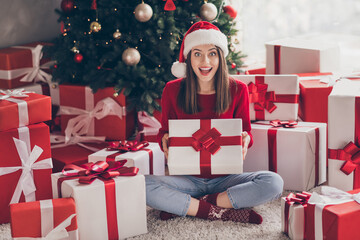 Obraz na płótnie Canvas Portrait of her she nice attractive charming cheerful cheery glad girl sitting on carpet floor holding in hands pile stack giftboxes christmastime in light decorated house interior indoor
