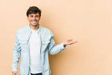 Young cool man showing a copy space on a palm and holding another hand on waist.