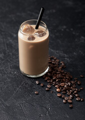 Glass of iced cold coffee and milk with frew raw coffee beans on black background.