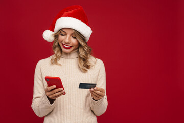 Excited girl in Santa Claus hat showing cellphone and credit card