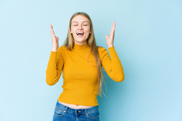 Young blonde woman isolated on blue background laughs out loudly keeping hand on chest.