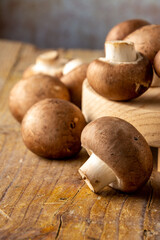 Top view of portobello mushrooms on wooden board and rustic table, with selective focus, dark background, in vertical with copy space
