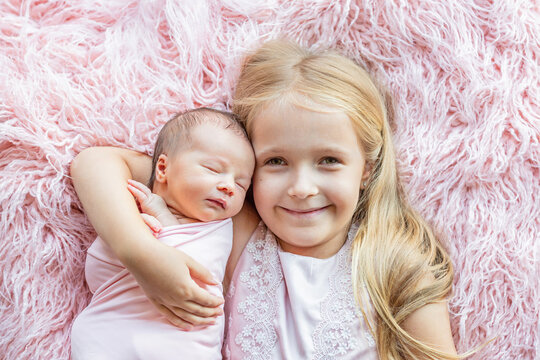 Little girl and her newborn sister. Toddler kid meeting new sibling. Cute girl and new born baby relax in a home bedroom. Family with two children at home. Love, trust and tenderness concept