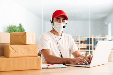 Male delivery assistance in face mask working with packages and laptop