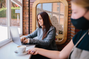 happy young girl, working with a laptop in a cafeteria while the barista serves her a coffee cup