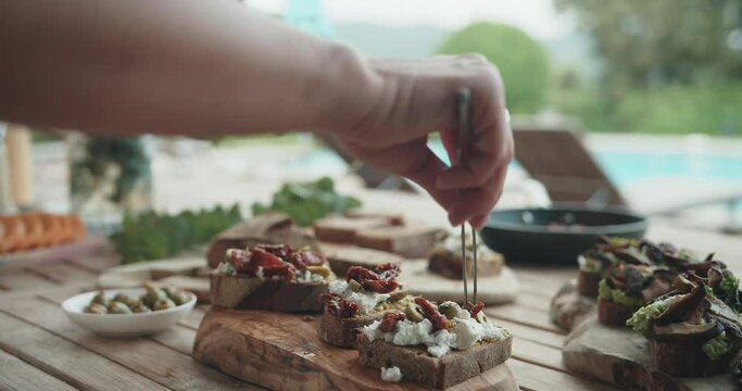Female chef puts sun-dried tomatoes in olive oil on the bruschetta on a wooden table at the summer kitchen.Cook chef cooking tasty and healthy delicious food outside. Cooking at home,food or cook vlog