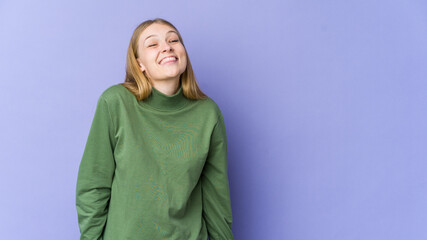 Young blonde woman isolated on purple background laughs and closes eyes, feels relaxed and happy.