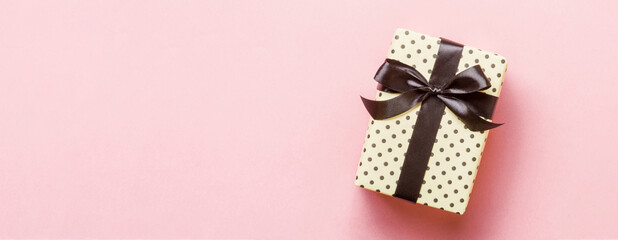 Gift box with black bow for Christmas or New Year day on pink background, top view with copy space