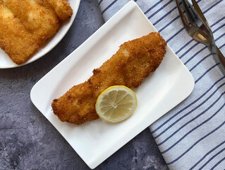 Breaded cod fish fillets, also known as Kabeljau. The fish is coated in egg, flour and breadcrumbs, then deep fried to golden brown and served with lemon.