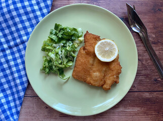 Breaded cod fish fillet, also known as Kabeljau. The fish is coated in egg, flour and breadcrumbs, then deep fried to golden brown and served with green salad with Vinaigrette and lemon.