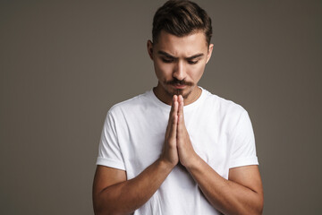 Image of tense unshaven guy posing and holding palms together