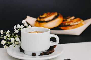 Sweet roll with poppy seeds and black cup of espresso on a white table. Breakfast at home - black coffee and bun with poppy seeds