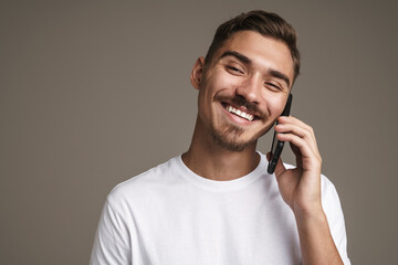 Image of joyful unshaven guy smiling and talking on cellphone