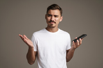 Image of confused guy showing gesturing while holding cellphone