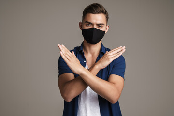 Image of caucasian displeased guy in face mask showing stop sign