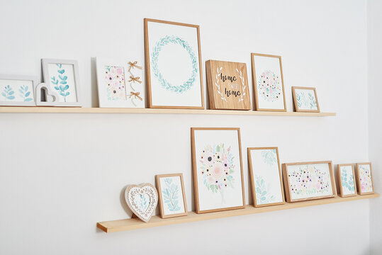 Watercolor flowers pictures on wall. Shelves with picture frames on white background. Creative workshop decor. Painting hobby and leisure concept. Inspiration and creativity. Room interior.