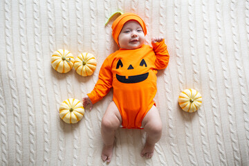 Fototapeta premium High Angle View Of Baby In Pumpkin Costume. Happy Kid two months old in orange Halloween costume on bed