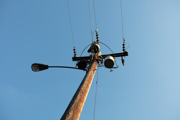 Electrical Power line transformers and street light on a pole against an afternoon blue sky