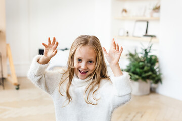 Little girl with blonde hair in a white sweater playing near the Christmas tree, laughing, smiling,