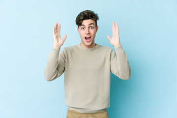 Young caucasian man isolated on blue background celebrating a victory or success, he is surprised and shocked.