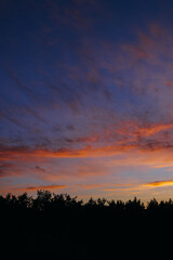 Breathtaking early sunrise over the forest with orange, goldlike and pink clouds.