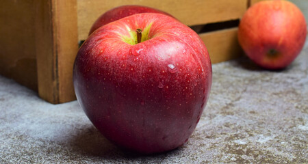 Red apple with water drops on light stone, in wooden box background