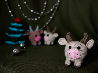 Beige crocheted toy bull cow in the foreground. In the background a green background, two other...
