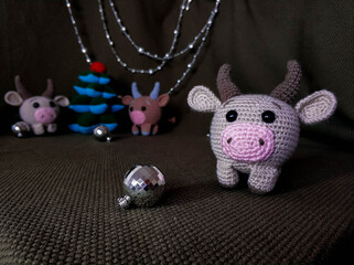 Beige crocheted toy bull cow in the foreground. In the background a green background, two other...