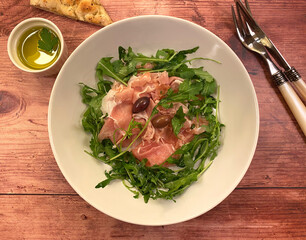 Prosciutto arugula salad appetizer. Prosciutto ham in very thin slices with arugula, olives and balsamic vinaigrette. 