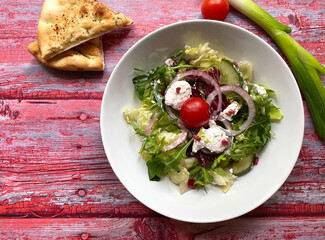 Greek style salad with colorful vegetables, mixed greens, red onions, cucumber, tomato, herbs, crumbly feta cheese and vinaigrette. Perfect summer dinner. 