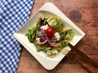 Greek style salad with colorful vegetables, mixed greens, red onions, cucumber, tomato, herbs, crumbly feta cheese and vinaigrette. Perfect summer dinner. 