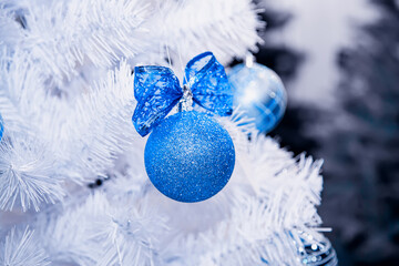 Fototapeta na wymiar Blue Christmas ball with glitter hangs on white artificial fir tree