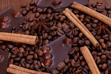 Chocolate bar with nuts on a wooden table with coffee beans and spices. Roasted coffee beans, cinnamon sticks and anise stars. Macro shot.