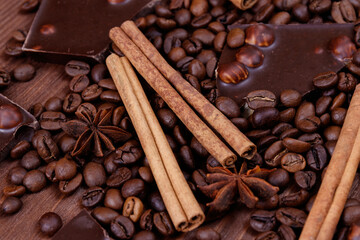 Chocolate bar with nuts on a wooden table with coffee beans and spices. Roasted coffee beans, cinnamon sticks and anise stars. Macro shot.